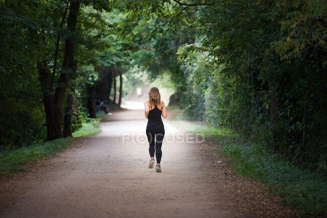 Joven mujer en forma huyendo haciendo deporte en un camino en el parque en un día soleado - foto de stock