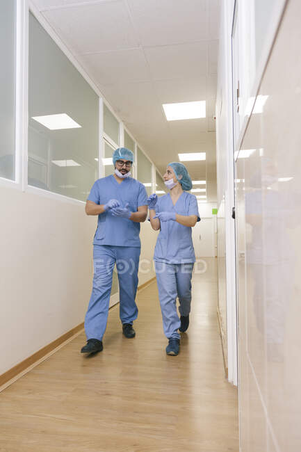 Коллеги хирурги мужчина и женщина беседуют во время ходьбы к операционной — стоковое фото