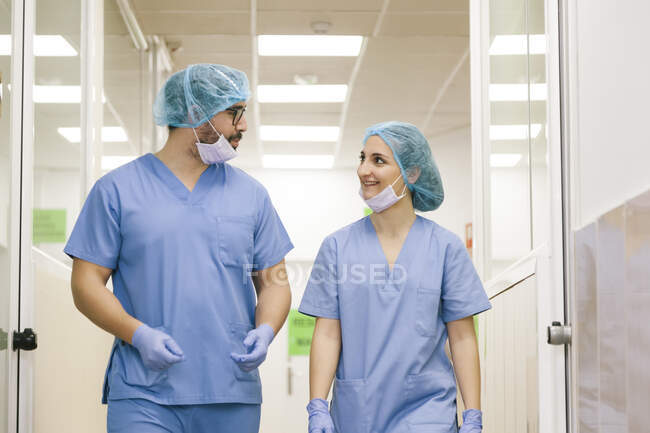 Companheiros cirurgiões homem e mulher bate-papo enquanto caminha em direção ao teatro cirúrgico — Fotografia de Stock