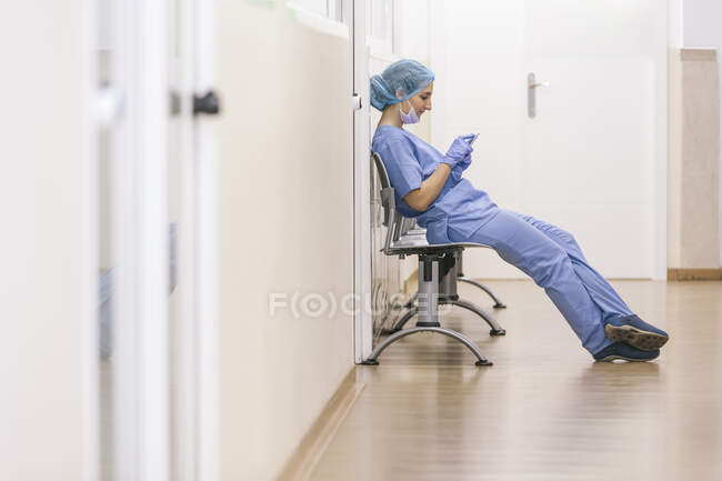 Female surgeon rests in a chair while checking messages on her smartphone — Stock Photo