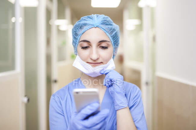 Cirurgiã feminina de pé no corredor enquanto verifica mensagens em seu telefone inteligente — Fotografia de Stock