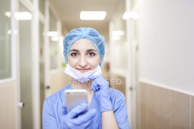 Хірург-жінка стоїть у коридорі, перевіряючи повідомлення на смартфоні. — стокове фото