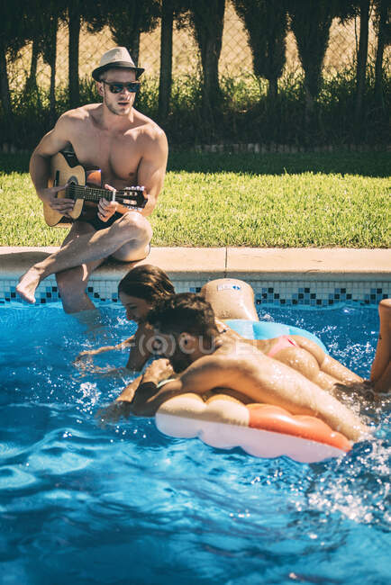 Hombres y mujeres relajándose junto a la piscina - foto de stock