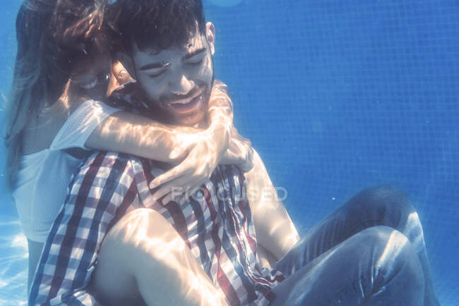 Femme embrassant l'homme dans des vêtements sous l'eau et souriant. — Photo de stock