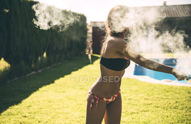 Menina bonita vestindo maiô posando com tocha de fumaça na festa na piscina no quintal. — Fotografia de Stock