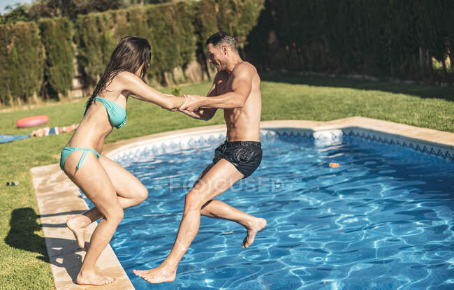 Chico tirando de su novia en piscina - foto de stock