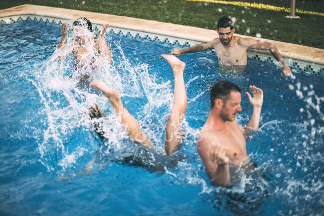 Amigos saltando en la piscina y nadando - foto de stock