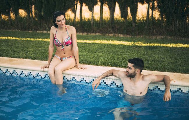 Guy schwimmen und mädchen sitzen auf pool side — Stockfoto