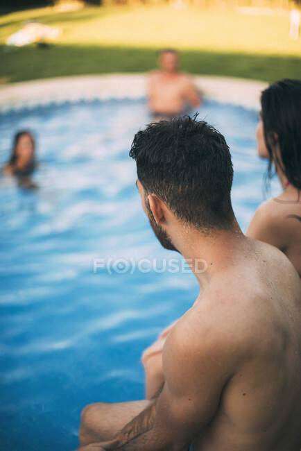 Amigos sentados en el borde de la piscina - foto de stock