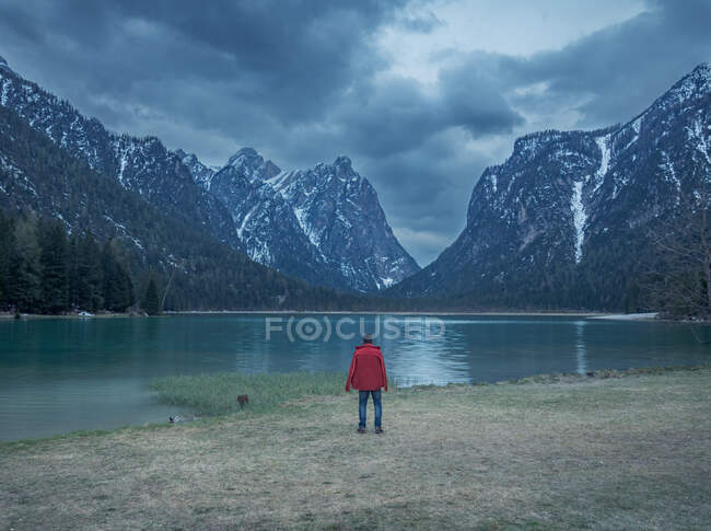 Visão traseira do viajante adulto tirar fotos de cume da montanha enquanto está em pé na costa do lago calmo na natureza — Fotografia de Stock