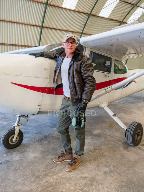 Confident pilot standing next to retro plane in hangar — Stock Photo