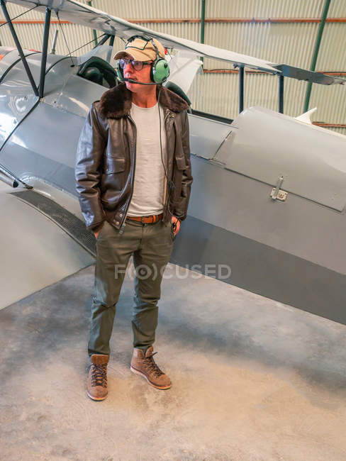 Pilote confiant debout à côté de l'avion rétro dans le hangar — Photo de stock