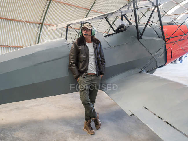 Confident pilot leaning on retro plane in hangar — Stock Photo