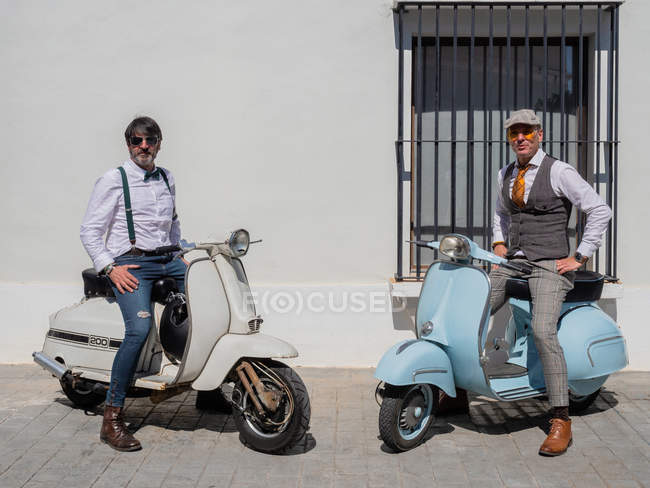 Hipsters positivos de meia-idade em roupas elegantes com motos retro olhando para a câmera em dia ensolarado — Fotografia de Stock