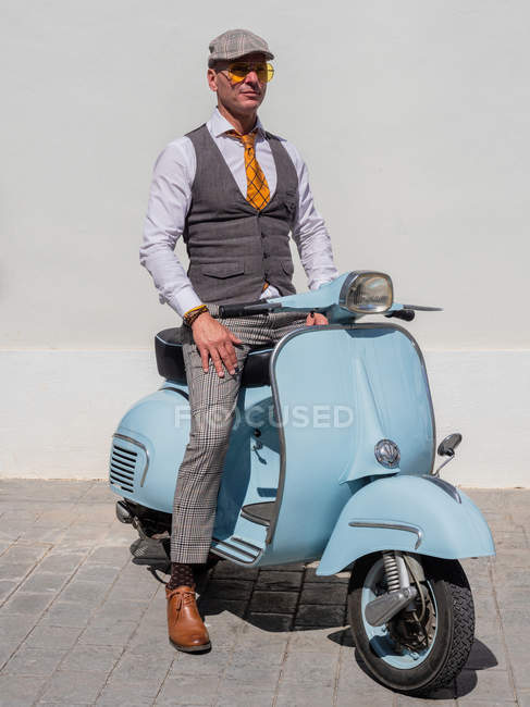 Позитивный хипстер средних лет в элегантной одежде с ретро мотоциклом, смотрящим в солнечный день — стоковое фото