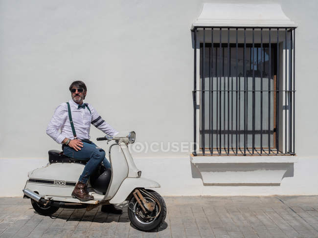 Positive middle-aged hipster in elegant clothes with retro motorbike looking away in sunny day — Stock Photo
