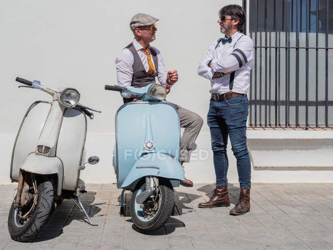 Позитивні середнього віку хіпстери в елегантному одязі з ретро мотоциклами розмовляють один з одним в сонячний день — стокове фото