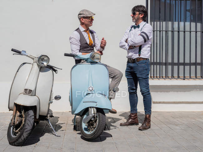 Positivi hipster di mezza età in abiti eleganti con moto retrò che si parlano nella giornata di sole — Foto stock