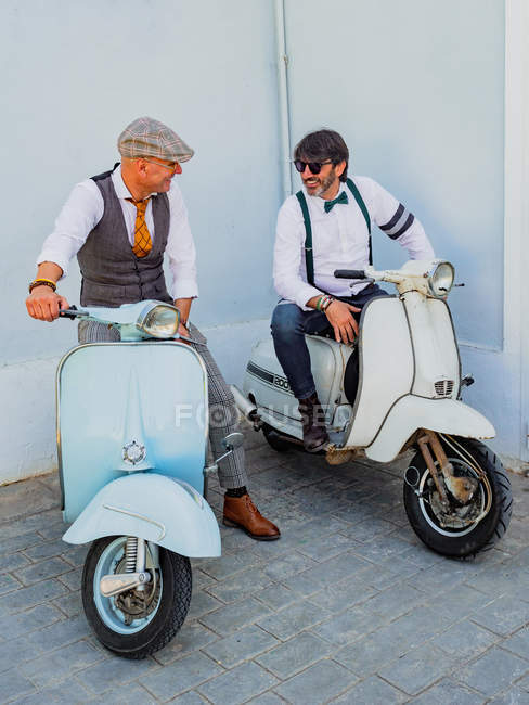 Позитивные хипстеры средних лет в элегантной одежде с ретро мотоциклами, смотрящими друг на друга в солнечный день — стоковое фото