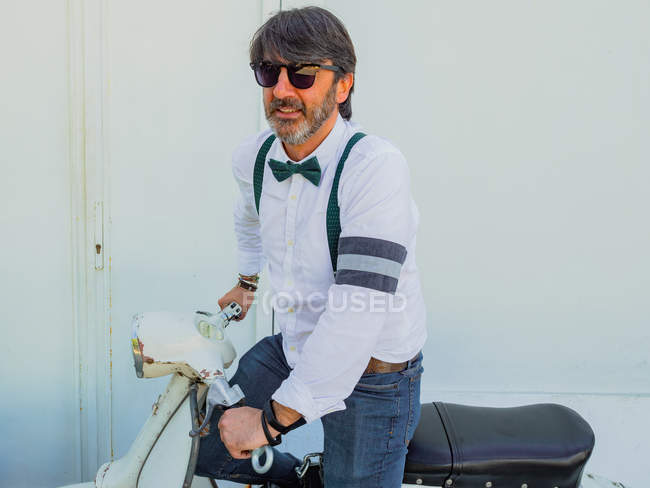 Positive middle-aged hipster in elegant clothes with retro motorbike looking away in sunny day — Stock Photo