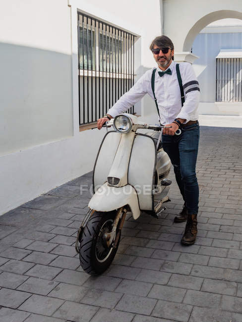 Positive middle-aged hipster in elegant clothes with retro motorbike looking at camera — Stock Photo