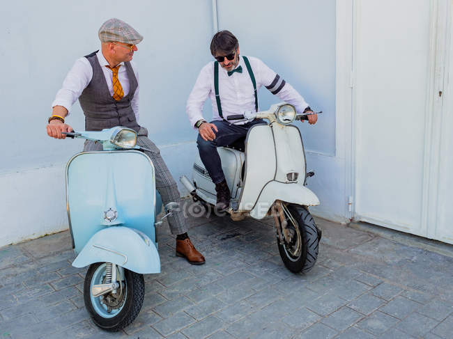 Positive middle-aged hipsters in elegant clothes with retro motorbikes looking at each other in sunny day — Stock Photo