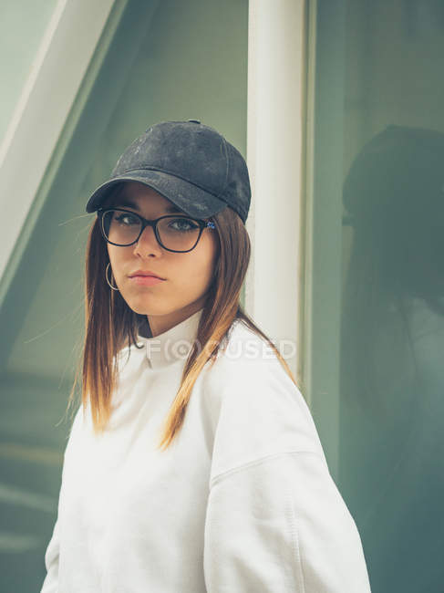 Junge moderne Hipsterin in lässiger Kleidung vor dem Hintergrund einer geometrischen Wand, die in die Kamera blickt — Stockfoto