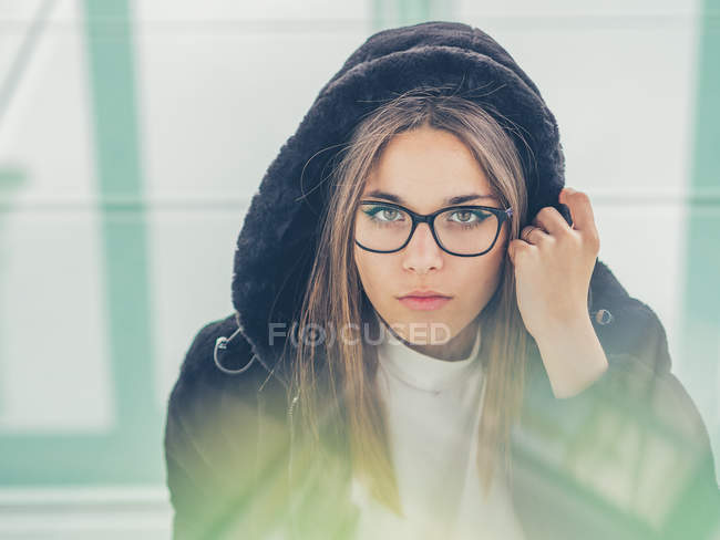 Joven hipster femenino moderno en ropa casual sobre fondo de gafas geométricas mirando a la cámara - foto de stock