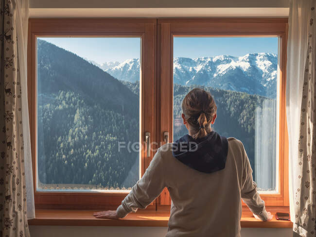 Mujer anónima mirando montañas desde la ventana - foto de stock