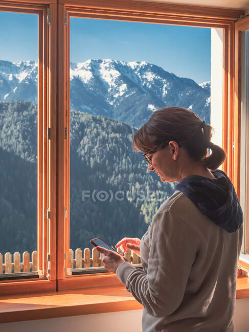 Femme naviguant smartphone près de la fenêtre — Photo de stock