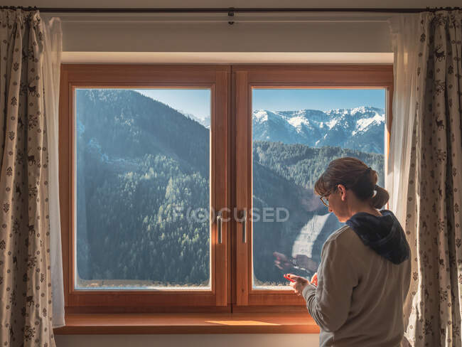 Женщина просматривает смартфон возле окна — стоковое фото