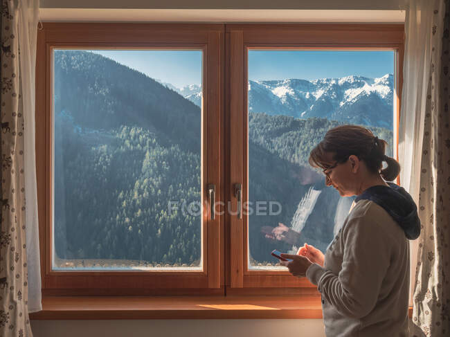 Woman browsing smartphone near window — Stock Photo