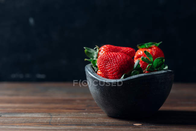 Fresas frescas maduras en un tazón de hormigón negro sobre fondo de madera - foto de stock