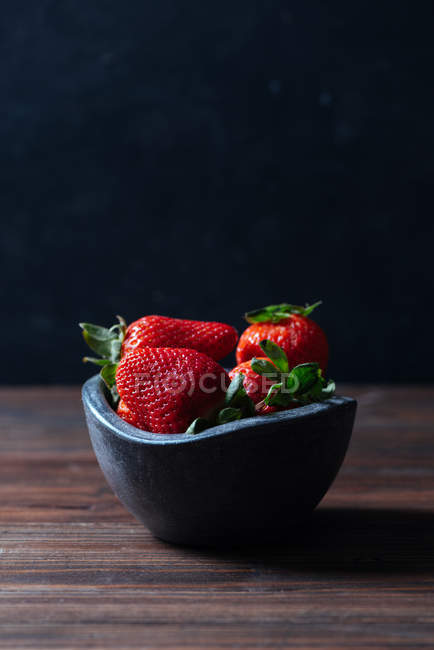 Frische reife Erdbeeren in schwarzer Betonschale auf Holzhintergrund — Stockfoto