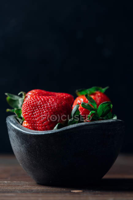 Fresas frescas maduras en un tazón de hormigón negro sobre fondo de madera - foto de stock
