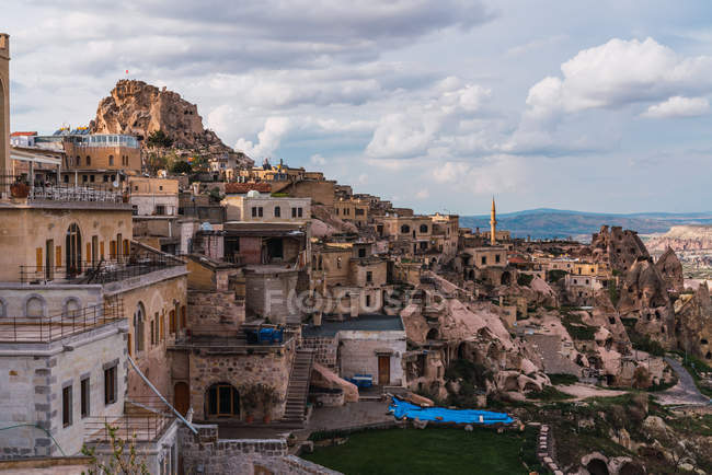 Обветшалые каменные дома старого города, расположенные на грубой горе против облачного неба Каппадокии, Турция — стоковое фото