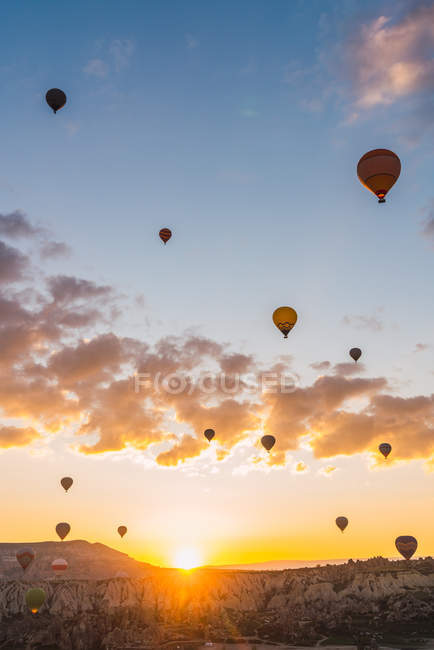 Воздушные шары, летящие против горного хребта и солнечного закатного неба во время фестиваля в Каппадокии — стоковое фото