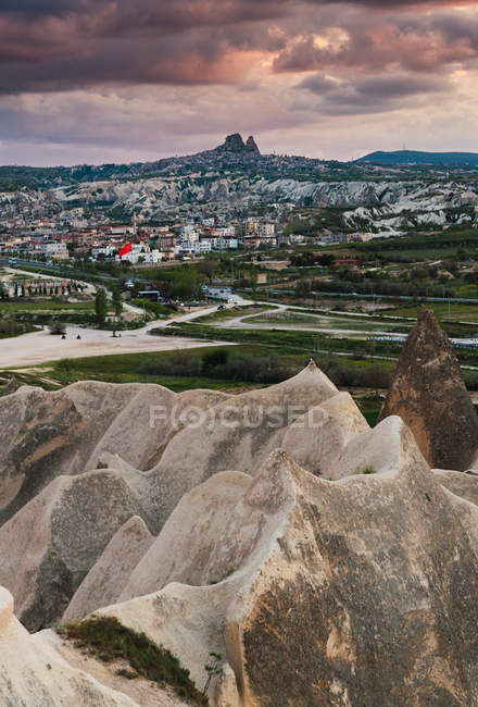 Cima di ruvida formazione rocciosa in campagna sorprendente contro cielo coperto e città lontana in Cappadocia, Turchia — Foto stock
