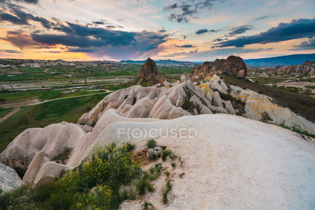 Pico de formação rochosa em incrível campo contra céu nublado e cidade distante na Capadócia, Turquia — Fotografia de Stock