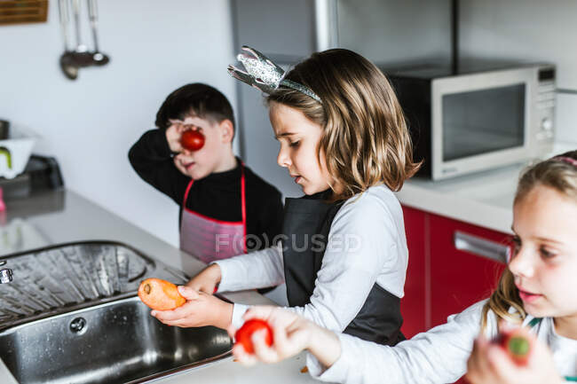 Kleine Mädchen und Jungen schneiden und schälen reifes Gemüse beim gemeinsamen Kochen von gesundem Salat in der Küche — Stockfoto