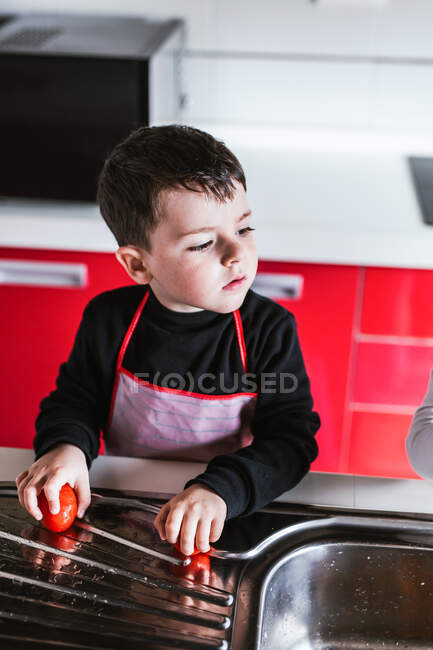Niño sosteniendo tomates para cocinar ensalada saludable en la cocina - foto de stock
