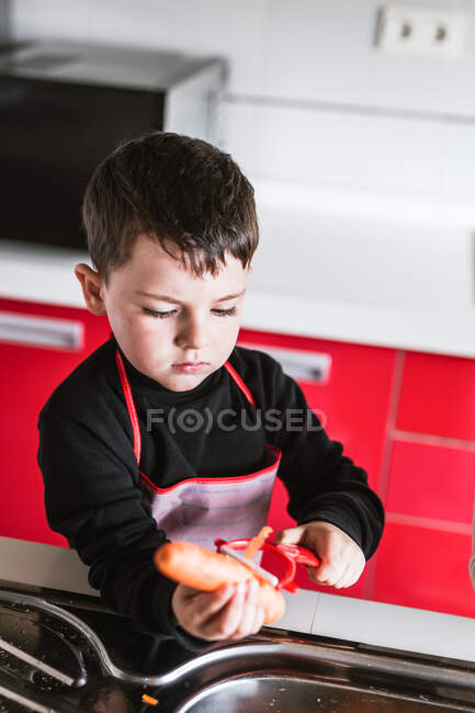 Garçon éplucher la carotte tout en cuisinant une salade saine dans la cuisine — Photo de stock