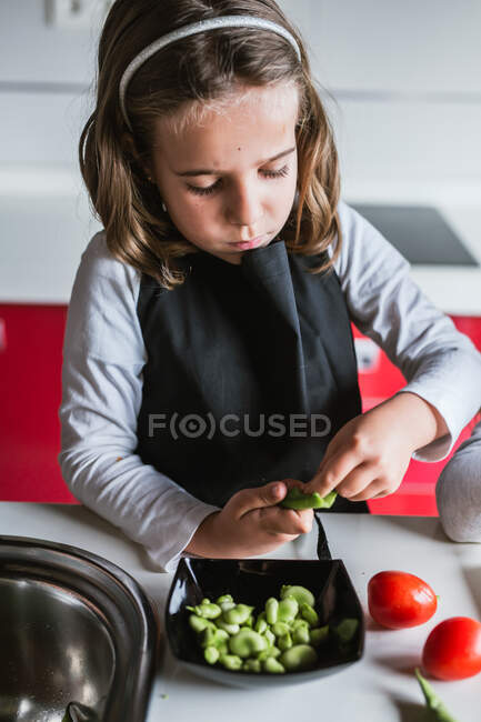 Menina descascando feijões maduros enquanto cozinham salada saudável na cozinha juntos — Fotografia de Stock