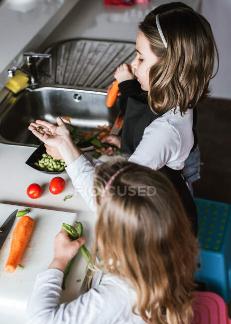 Meninas e meninos cortando e descascando legumes maduros enquanto cozinham salada saudável na cozinha juntos — Fotografia de Stock