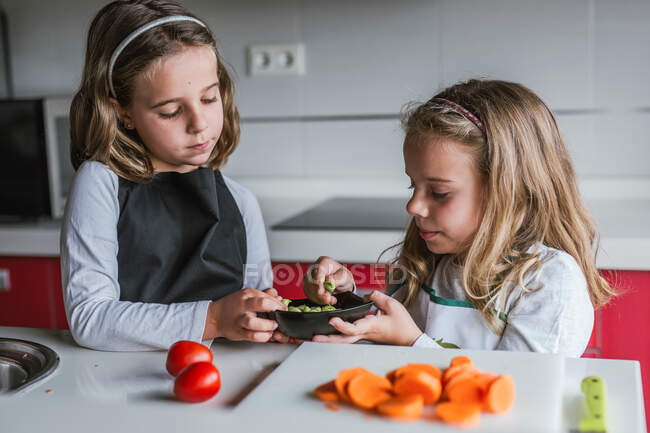 Kleine Mädchen schälen reifes Gemüse, während sie in der Küche gemeinsam gesunden Salat zubereiten — Stockfoto