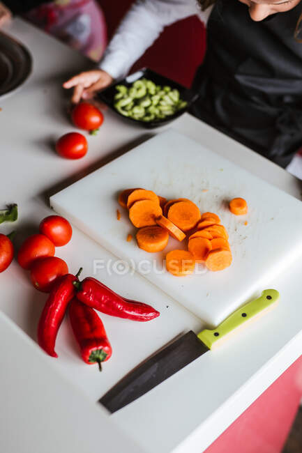 Вид на урожай анонімних маленьких дівчаток і хлопчика, які ріжуть і очищають стиглі овочі, готуючи здоровий салат на кухні разом — стокове фото