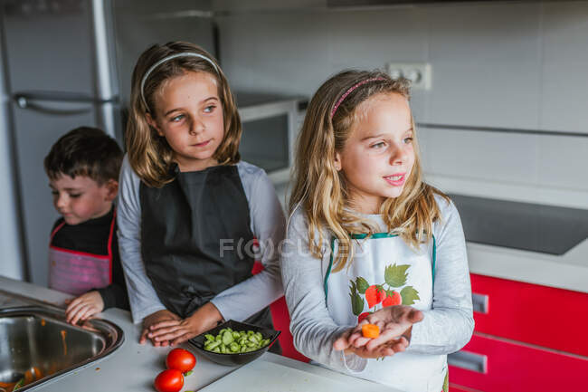 Petites filles pelant des légumes mûrs tout en cuisinant une salade saine dans la cuisine ensemble — Photo de stock