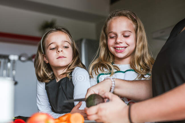Anonymous adult showing little girls to cook healthy salad in kitchen together — Stock Photo