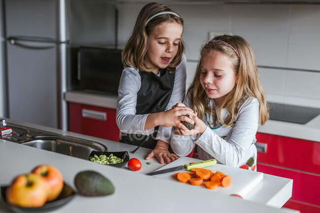Menina demonstrando metade do abacate maduro para câmera enquanto estava na cozinha olhando para a câmera — Fotografia de Stock