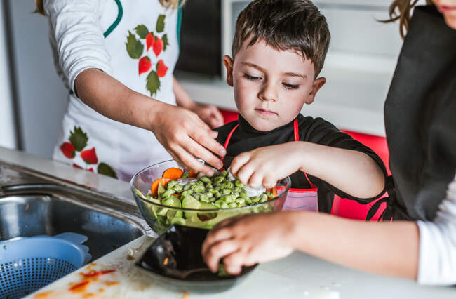 Petites filles et garçons coupant et épluchant des légumes mûrs tout en cuisinant une salade saine dans la cuisine ensemble — Photo de stock